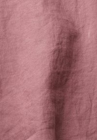 Tissu en lin rose pâle avec une texture de tissage visible et des plis naturels créant des ombres et des reflets subtils.