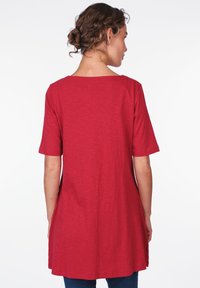 Red, short-sleeve tunic top with a relaxed fit. Made of soft fabric, featuring a round neckline and slightly elongated back.