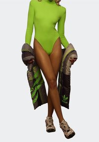Neongrön ribbad bodysuit med hög skärning, tillsammans med en mönstrad svart och grön puffjacka. Krämfärgade och svarta chunky sneakers.