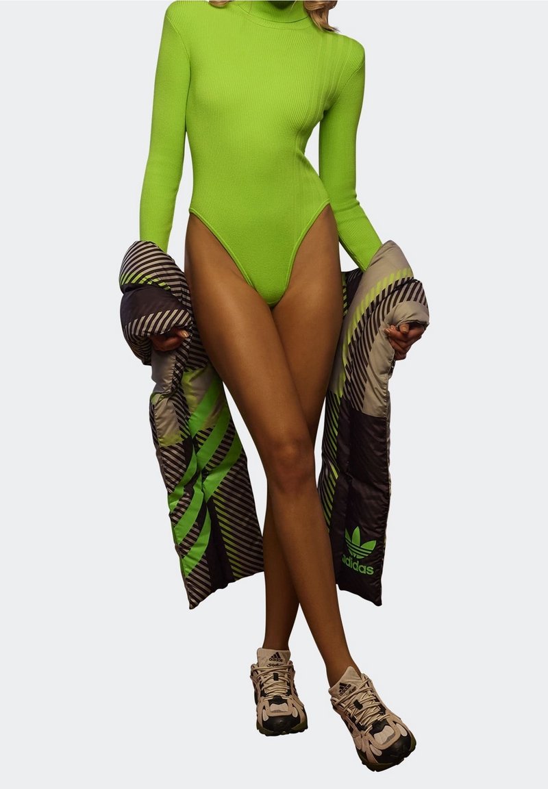 Neongrön ribbad bodysuit med hög skärning, tillsammans med en mönstrad svart och grön puffjacka. Krämfärgade och svarta chunky sneakers.