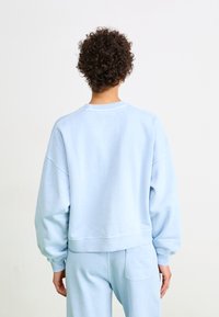 Sweatshirt bleu clair au design décontracté, avec des coutures d'épaule tombantes, des poignets côtelés et un col rond. Texture douce, détails minimalistes.