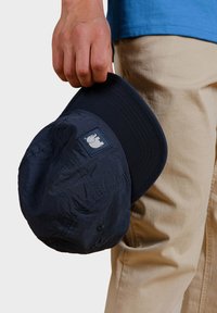 Tmavě modrá baseballová čepice držena v ruce, s texturovanou tkaninou, pevným kšiltem a logem s designem slona.