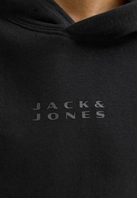 Felpa nera con cappuccio caratterizzata da una consistenza morbida e da un logo "JACK & JONES" in rilievo di colore grigio scuro ben visibile.