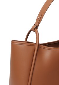 Brązowa skórzana torba typu bucket o gładkiej fakturze, solidnym pasku na ramię i minimalistycznym designie. Górna krawędź wykończona dyskretnym szwem.