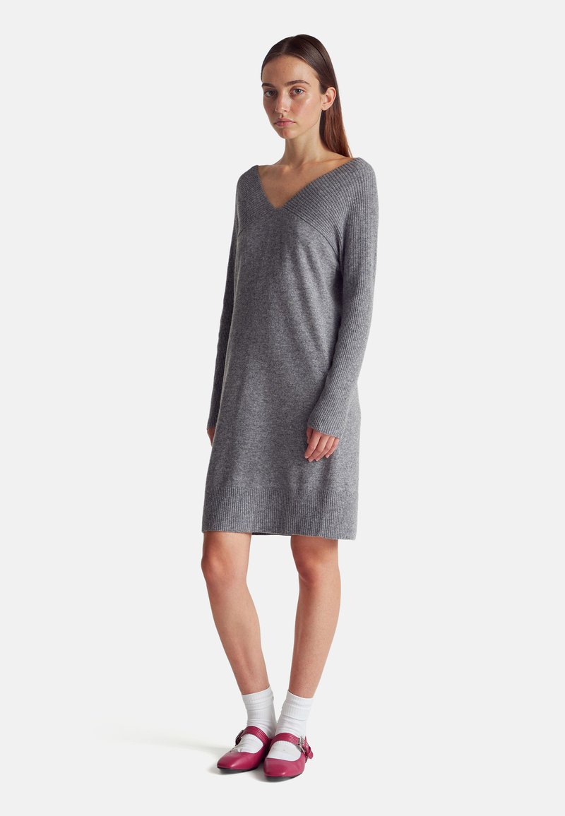 Šedé pletené šaty s V výstřihem, dlouhými rukávy a žebrovanými detaily na manžetách a spodním lemu. Spárováno s růžovými botami a bílými ponožkami.