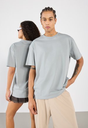 T-shirts oversize gris clair, en tissu doux, col rond, manches courtes. Un modèle se tient devant, l'autre à l'arrière, portant un short.