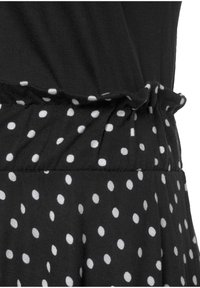 Schwarzes Kleid mit geraffter Taille, bestehend aus einem Oberteil aus einfarbigem schwarzen Stoff und einem Rockteil mit großen weißen Punkten auf schwarzem Hintergrund.