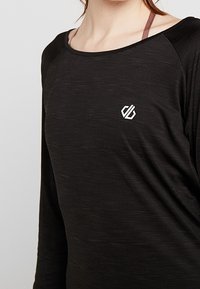 Chemise noire à manches longues avec un col arrondi, fabriquée dans un tissu texturé, comportant un petit logo blanc sur la zone gauche de la poitrine.