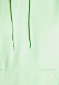 Sudadera verde claro con capucha, que presenta cordones con terminales metálicos, textura suave y detalle de bolsillo tipo canguro. Diseño mejorado para mayor comodidad.