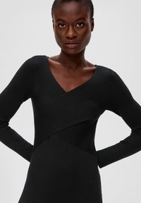 Schwarzes, geripptes Kleid mit V-Ausschnitt und langen Ärmeln, das ein überlappendes Design am Oberkörper aufweist, das Textur und strukturierten Schnitt betont.