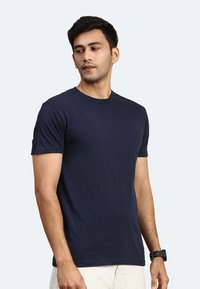 Marineblaue Baumwoll-T-Shirt mit kurzen Ärmeln, Rundhals, taillierter Schnitt, glatte Textur, getragen mit hellen Shorts.