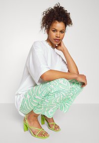 T-shirt branco oversized, calças verdes com padrão de zigzag e sandálias altas verdes com salto bloco.