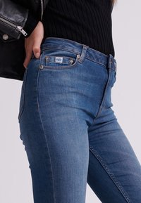 Jeans de denim azul con un ajuste slim, que cuentan con una cintura de altura media, diseño de cinco bolsillos y una pequeña etiqueta de la marca en el bolsillo delantero.