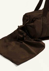 Hnědá nylonová taška přes rameno s nařasenou, rozšiřitelnou kapsou. Má dvojité ramenní popruhy a zipové uzavření. Texturovaný, měkký povrch.