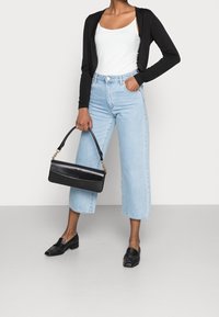 Svart kofta över en vit linne, ljusblå vida jeans, svarta loafers och en svart handväska med ett guldkedjesmycke.