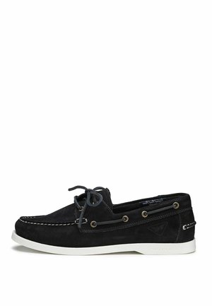 Scarpa da barca in suede nero con suola in gomma bianca, cuciture a contrasto e design con lacci. Presenta occhielli in metallo e una superficie liscia.