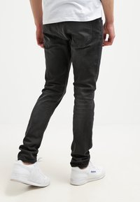 Svarta denimjeans med slim fit, med en medelhög midja och bakfickor, i kombination med vita sneakers. Tyget har en jämn yta.