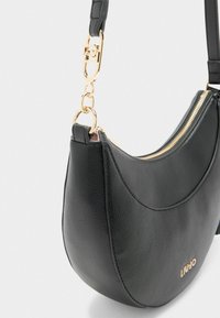 Borsa a tracolla nera in pelle con forma curva, hardware dorato, chiusura con zip e logo impresso sul davanti.