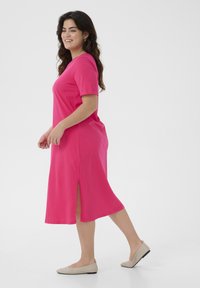 Robe rose à manches courtes avec un col rond et des fentes sur les côtés. Fabriquée en tissu doux et léger, atteignant le mollet. Associée à des ballerines beiges.