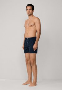 Tmavě modré kostičkované trenky s elastickým pasem a předním zapínáním na knoflík, prezentované na modelu stojícím na neutrálním pozadí.