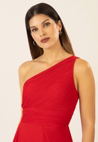 Rotes One-Shoulder-Kleid mit Faltenstruktur, tailliertem Oberteil und fließendem Rock. Verfügt über einen breiten Taillenbund und einen glatten Stoffabschluss.