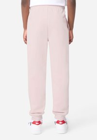 Κρεμ δροσερές φόρμες από απαλό ύφασμα με ελαστική μέση και μανσέτες στους αστραγάλους. Συνδυάζονται με λευκά παπούτσια με κόκκινες λεπτομέρειες.