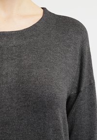 Ciemnoszary sweter dzianinowy z okrągłym dekoltem, charakteryzujący się miękką fakturą i luźnym krojem. Widoczne detale szycia wzdłuż krawędzi.