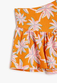 Orange stof med en tekstureret overflade, der har pink og blå tropiske blomstermønstre. Designet inkluderer en sammensamlet flæse detalje forneden.