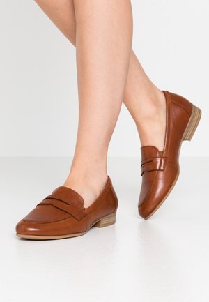 Mocassins en cuir marron avec un petit talon empilé, présentant un design cousu et une large sangle en travers à l'avant. Texture lisse.