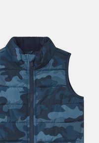 Granatowa, pikowana kamizelka z wysokim kołnierzem, z wzorem w kamuflaż w różnych odcieniach niebieskiego, z zapięciem na zamek błyskawiczny z przodu.