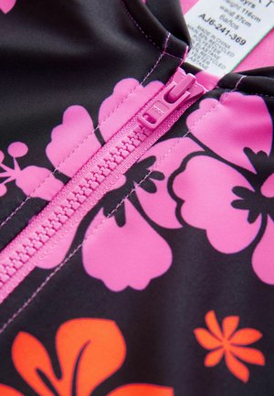 Tela negra con grandes patrones florales en tonos rosa y naranja, con un zipper rosa en la parte delantera. Etiqueta visible cerca del zipper.