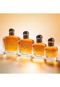 Fyra klara glasparfymflaskor med rundade lock, fyllda med bärnstenfärgad vätska, märkta "Stronger with You" och "Emporio Armani."