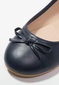 Ballerine in pelle blu navy con punta arrotondata e piccolo dettaglio a fiocco. Foderato internamente con materiale morbido e suola flessibile beige.
