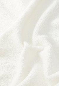 White towel with a soft, plush texture; fabric appears textured with loops; draped, creating gentle folds and shadows.