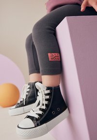 Leggings gris côtelés avec une étiquette rose "Minnie Mouse" assortis à des baskets montantes noires avec des lacets blancs et une semelle en caoutchouc.