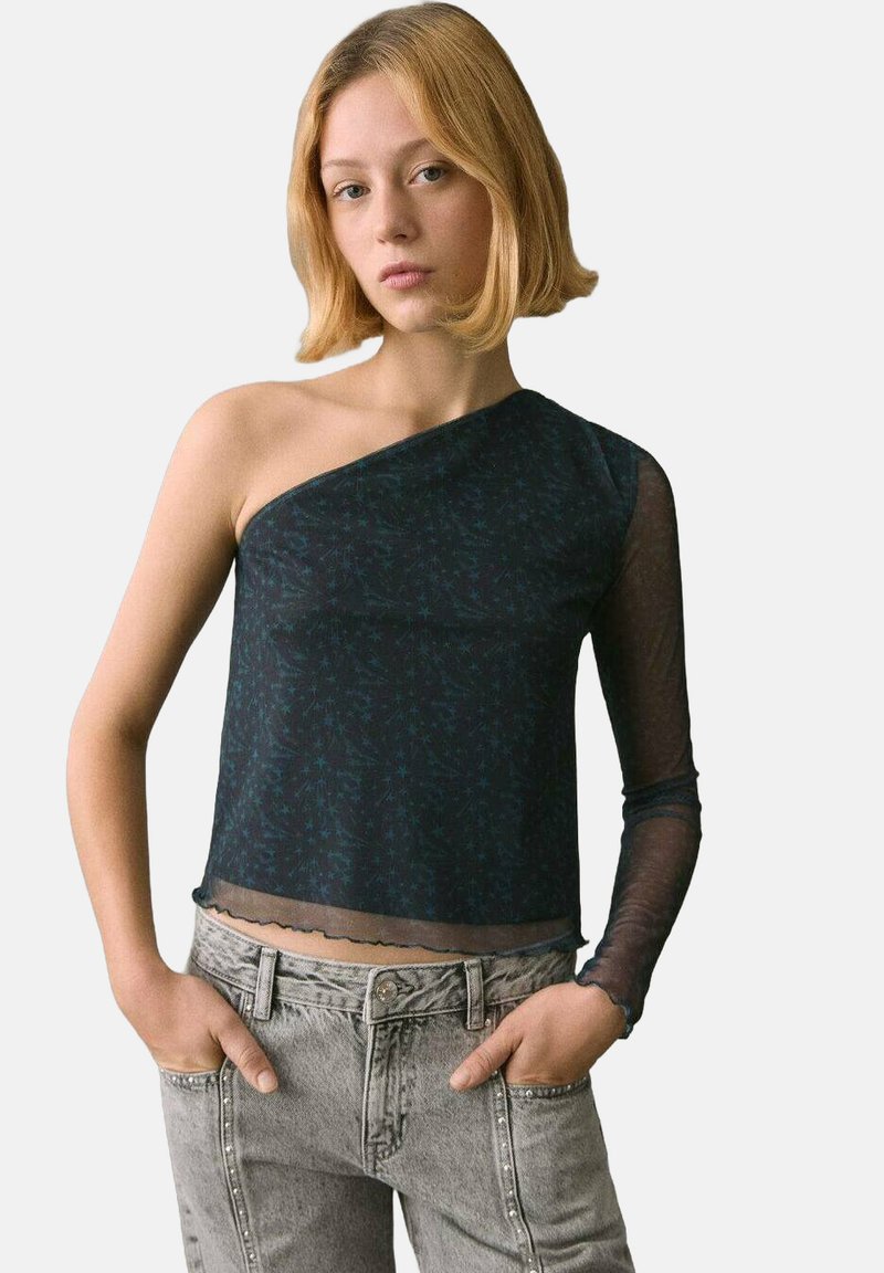 Asymmetrisches schwarzes Oberteil mit transparentem Ärmel, floralem Muster, taillierter Passform und gewelltem Saum, kombiniert mit hoch taillierten grauen Denim-Jeans.