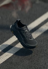 Chaussure de sport noire avec un dessus texturé, design à lacets, semelle rembourrée et semelle extérieure Vibram, avec des perforations pour la respirabilité.