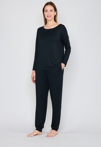 Zwart lang mouwen top en broek set gemaakt van zachte stof, met een relaxed fit, zijzakken en elastische manchetten, tentoongesteld op een model zonder schoenen.