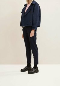 Marinblå kort jacka med dubbelknäppning, matchad med marinblå byxor och svarta loafers. Randig rosa skjorta synlig under.