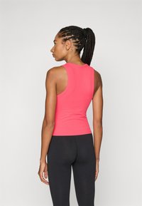 Top aderente senza maniche in cotone fucsia con una texture liscia e scollo rotondo, abbinato a leggings neri, visto da dietro.