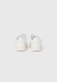 Pair of white low-top sneakers with flat soles, viewed from the back on a plain white background.