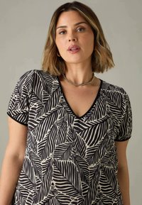 Svart och krämfärgad kortärmad klänning med V-ringning, som har ett lövmönster och en strukturerad tyg; kontrasterande kant vid ärmar och halsringning.