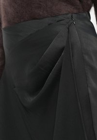 Gonna nera con un design strutturato caratterizzato da pieghe e chiusura con zip. Il tessuto ha una texture liscia, che enfatizza una silhouette sartoriale.