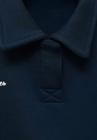 Polo di colore blu navy con tessuto testurizzato, colletto classico e un piccolo logo ricamato sul lato sinistro del petto.