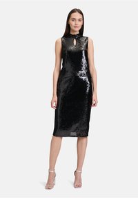 Schwarzes Pailletten-Kleid mit hohem Kragen, Schlüssel-Ausschnitt, enganliegender Silhouette und knie-langer Saumlinie. Tragen mit silbernen High Heels.