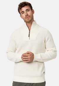 Suéter de punto color crema con cuello de media cremallera, patrón texturizado en el cuerpo, puños y dobladillo acanalados, con un pequeño detalle del logo.