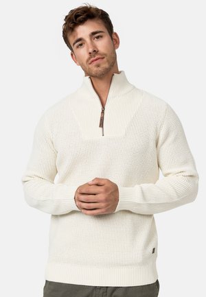 Suéter de punto color crema con cuello de media cremallera, patrón texturizado en el cuerpo, puños y dobladillo acanalados, con un pequeño detalle del logo.