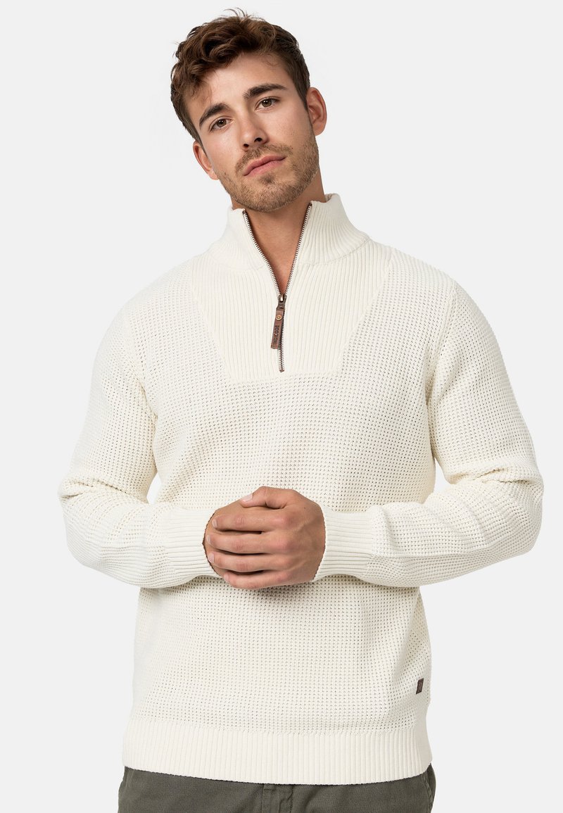 Cremfarbener Strickpullover mit einem Viertel-Reißverschluss-Kragen, strukturiertem Muster am Körper, gerippten Bündchen und Saum sowie einem kleinen Logo-Detail.