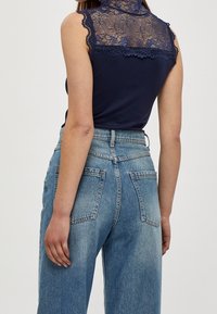 Haut sans manches bleu marine avec un dos en dentelle et un col montant, associé à un jean en denim taille haute bleu clair avec deux poches arrière.