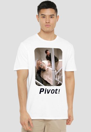 Man wearing white t-shirt with print of two people moving a couch up stairs and word "Pivot!" below the image.